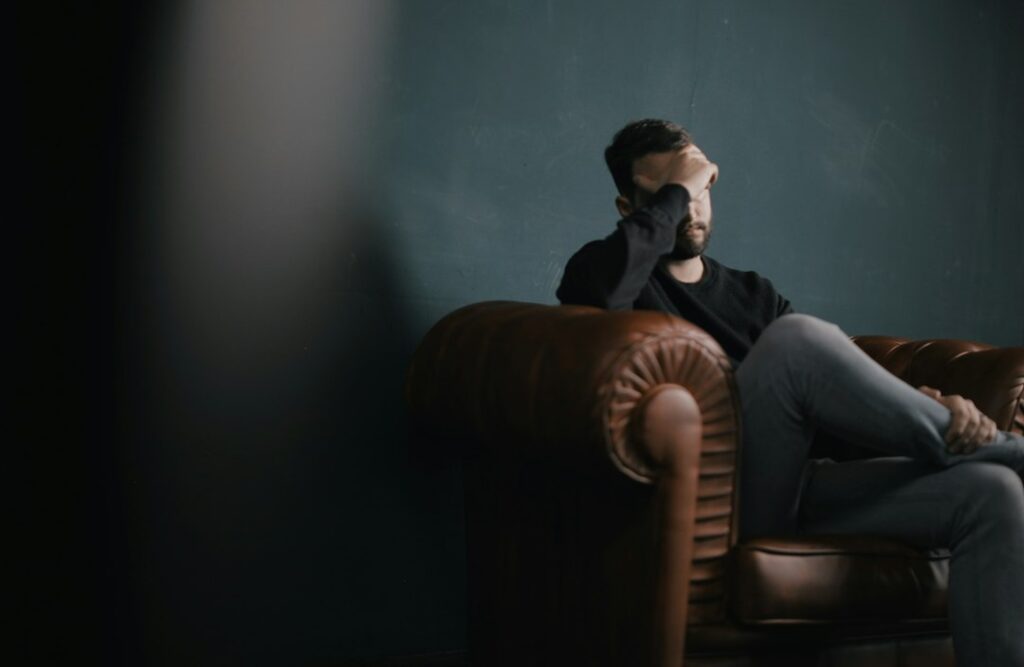 شخص يجلس وحيدًا على أريكة يضع يده على وجهه في حالة من القلق والتوتر بعد علاقة سامة
